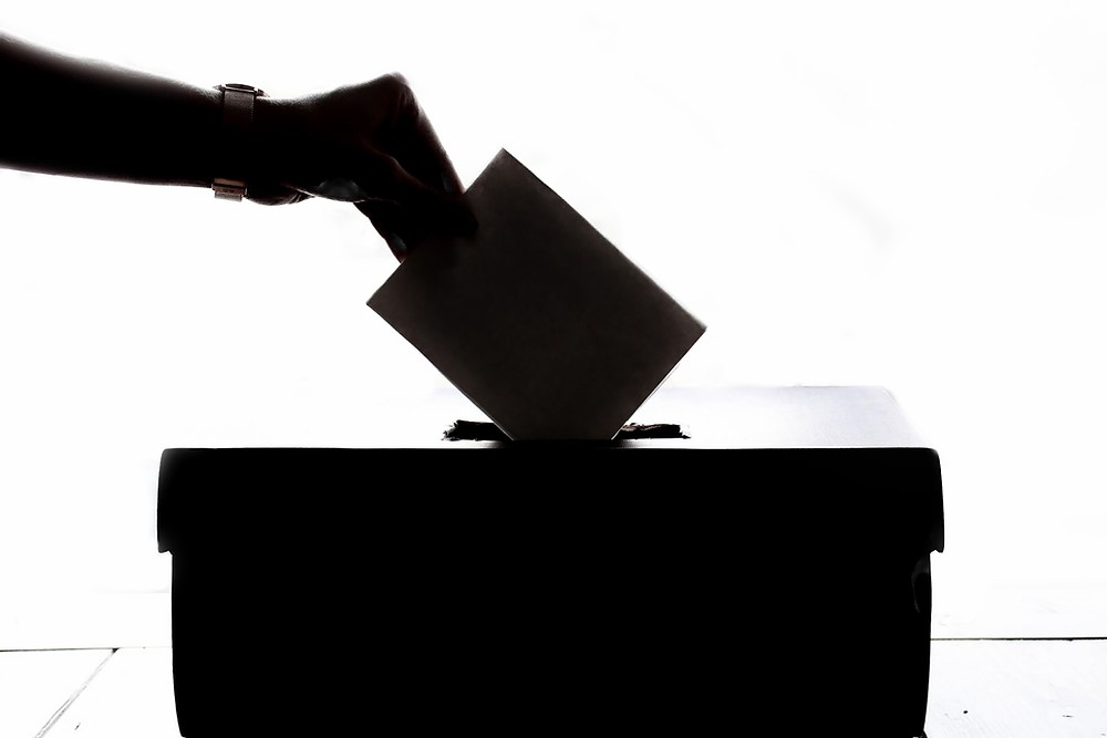 A silhouette of a hand putting a ballot into a ballot box.